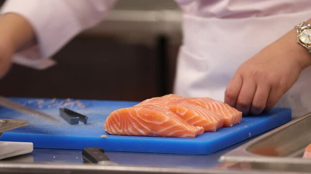Chef's hands meticulously remove pin bones from fresh fish fillets using tweezers. This precise technique on a blue cutting board ensures high-quality, boneless fish for cooking.