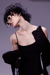 Fototapeta premium young woman with short black hair wearing round sunglasses and black dress posing in stylish contemporary fashion portrait studio setting