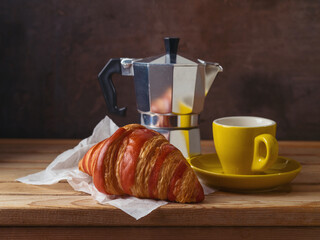 Still life with coffee cup, coffee pot and croissant on wooden table