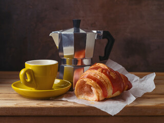 Still life with coffee cup, coffee pot and croissant on wooden table