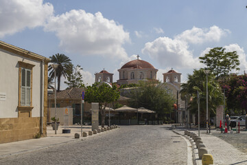Lefkosia, Cyprus - 25 June 2025: View of the sun-drenched cobblestone street leading towards the Church of Archangel Michael Trypiotis, its terracotta domes contrasting against the azure sky.