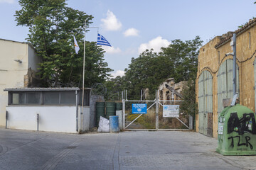 Lefkosia, Cyprus - 25 June 2025: View of a weathered gate, framed by buildings, flags, and foliage beneath a bright sky.