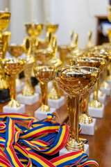 Close-up of golden trophies and colorful ribbons on a wooden table, prepared for an award ceremony.