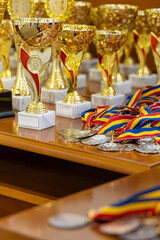 Golden trophies and a colorful pile of medals with ribbons on a wooden desk.