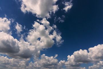 Fluffy white clouds float in deep blue sky during clear, sunny day, creating peaceful atmosphere.