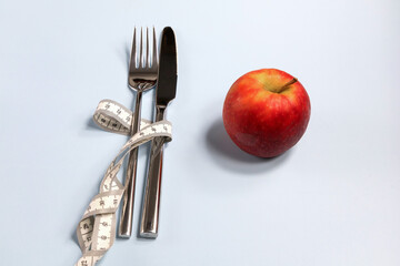 Fork and knife wrapped in a measuring tape and a red apple nearby