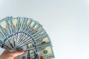 Person holding fan of US hundred dollar bills in hand against white background. Concept of wealth,...