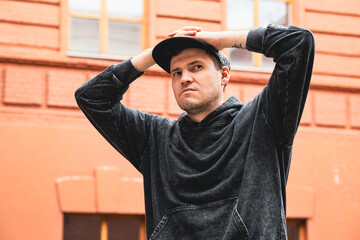 A man stands with hands on his head wearing a black hoodie and cap He looks contemplative in front...