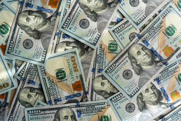 Hundred dollar banknotes spread out in chaotic pattern on wooden surface under bright sunlight....