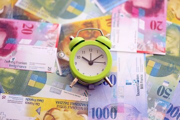 Swiss franc banknotes and alarm clock. The current francs money bills and clock lies on table