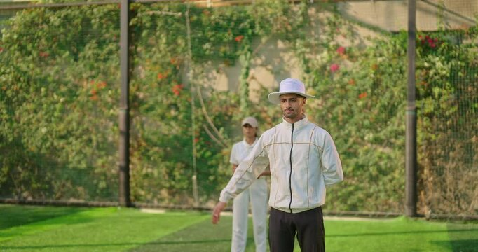 Indian asian young adult gen z bowler woman outdoor match play ground wear white uniform cap female lady girl skill do practice hit wicket stump umpire man show no ball with hand wide sign day time