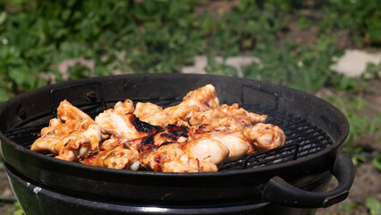 Grilling chicken thighs outdoors during a sunny day in a backyard setting while smoke rises from the barbecue grill