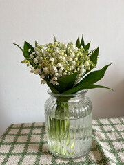 lilies of the valley stand in a vase on a green napkin