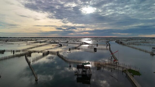Aerial drone footage of aquaculture fish and shrimp farms at sunset in Vietnam. Rows of ponds and water channels reflecting colorful twilight skies create a serene and atmospheric landscape