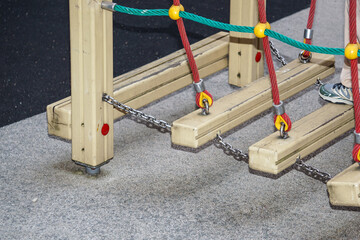 Close-up of suspended wooden playground bridge with ropes and chains. Child's foot on one plank. Safe adventure equipment for kids’ motor skills development