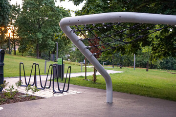 Modern playground climbing net structure and bike rack in a green city park at sunset. Urban recreational area for children and adults