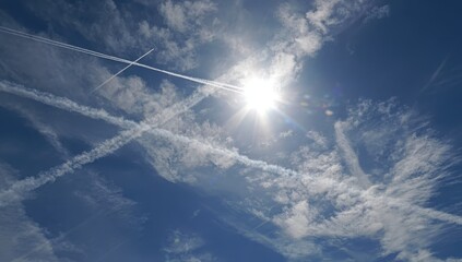 Azure sky crisscrossed with jet streams and wispy clouds, sun shining through