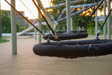 Modern playground climbing net structure and bike rack in a green city park at sunset. Urban recreational area for children and adults