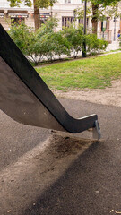 Modern playground with yellow slide and black tunnel tube structure in urban park. Sunny day, city skyscrapers in background. Children's outdoor play area