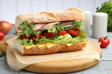 Tasty baguette sandwich with ham, cheese and vegetables on wooden table against grey background, closeup