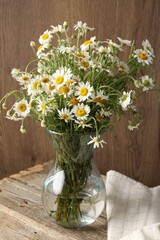 Beautiful chamomile flowers in glass vase on wooden table
