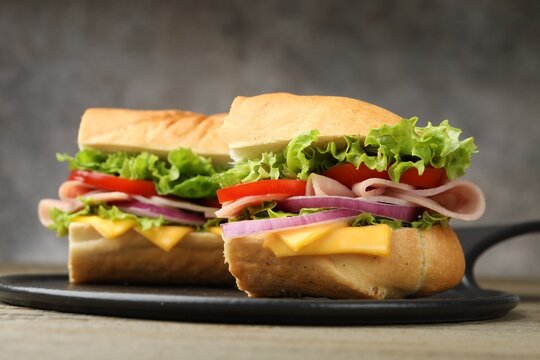 Pieces of tasty baguette sandwich with ham, cheese and vegetables on table against grey background, closeup