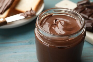 Tasty chocolate butter in glass jar on light blue table, closeup