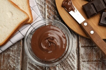 Tasty chocolate butter, pieces, knife and slices of bread on color wooden table, flat lay