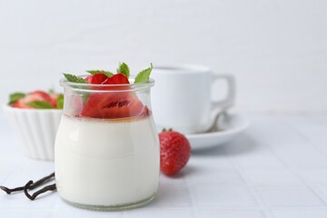 Tasty panna cotta with caramel, strawberries, mint, vanilla pods and coffee on white tiled table, closeup. Space for text