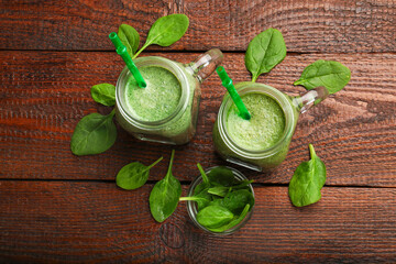 Tasty smoothie in mason jars and spinach leaves on wooden table, flat lay