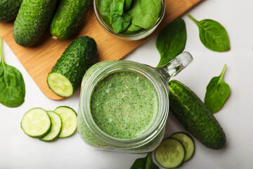 Tasty smoothie in mason jar, spinach leaves and cucumber on white table, flat lay