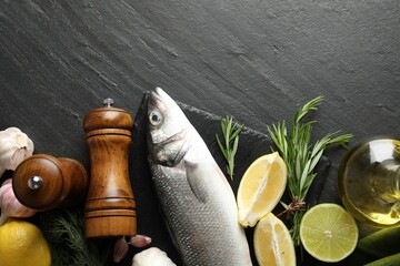 Fresh raw seabass fish with spices on black table, flat lay and space for text. Seafood delicacies