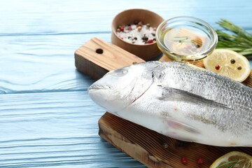 Fresh raw dourade fish with spices on blue wooden table, closeup and space for text. Seafood delicacies