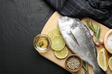 Fresh raw dourade fish with spices on black table, top view and space for text. Seafood delicacies