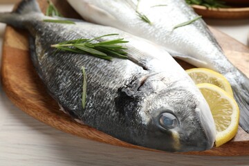 Fresh raw dorado fish, lemon slices, rosemary and spices on white wooden table, closeup. Organic...