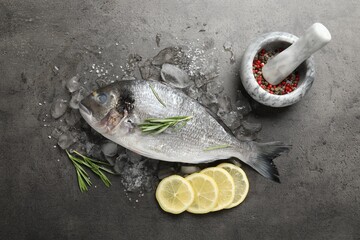 Fresh raw dorado fish, ice, lemon slices and rosemary on grey table, flat lay. Organic seafood