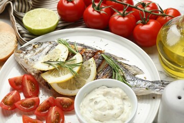 Tasty roasted dorado fish with sauce, tomatoes and lemon on white marble table, closeup. Homemade seafood dish