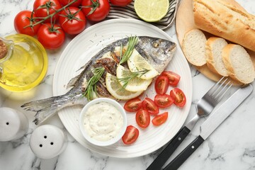 Tasty roasted dorado fish with bread, sauce, tomatoes and lemon on white marble table, flat lay. Homemade seafood dish