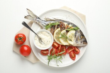 Tasty roasted dorado fish with sauce, tomatoes and lemon isolated on white, top view. Homemade seafood dish