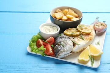 Homemade seafood dish. Tasty roasted dorado fish served with vegetables and sauce on light blue wooden table, closeup. Space for text