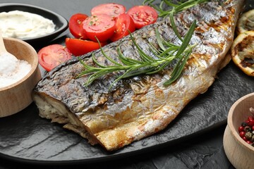 Tasty roasted mackerel served with spices and sauce on black table, closeup. Homemade seafood dish