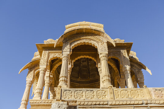 View of golden sandstone carvings of a historic chhatri rising against the clear blue sky, an architectural marvel of intricate design, Jaisalmer, Rajasthan, India.