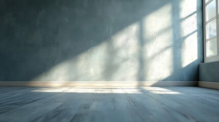 A spacious, empty room with a concrete wall and a large window, casting shadows on the floor.