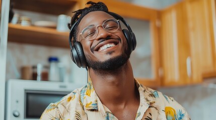 Naklejka premium Happy man wearing wireless headphones and listening to music in kitchen