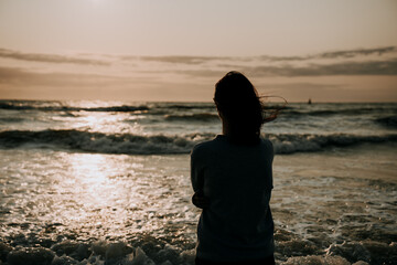 A girl stands and looks at the sunset at the sea