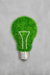 Eco-friendly concept featuring a green grass lightbulb on a gray concrete background symbolizing sustainable energy.