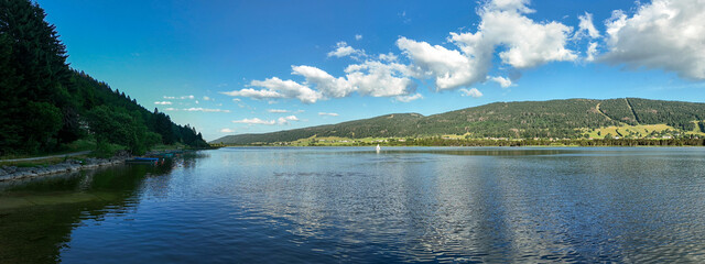 Summer Panorama of Lac des Rousses with Sailboat and Forest Shoreline – Jura, France