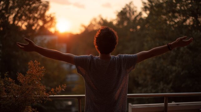 Young man with arms outstretched breathing in fresh air during sunrise at the balcony. boy enjoying nature - Powered by Adobe