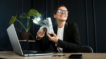 Confident middle-aged businesswoman holds a stack of money in a modern office. Represents...