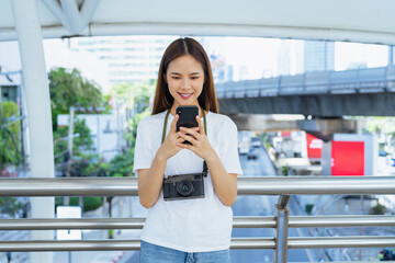 Cheerful beautiful Asian woman using smartphone and camera with looking for tourist attractions